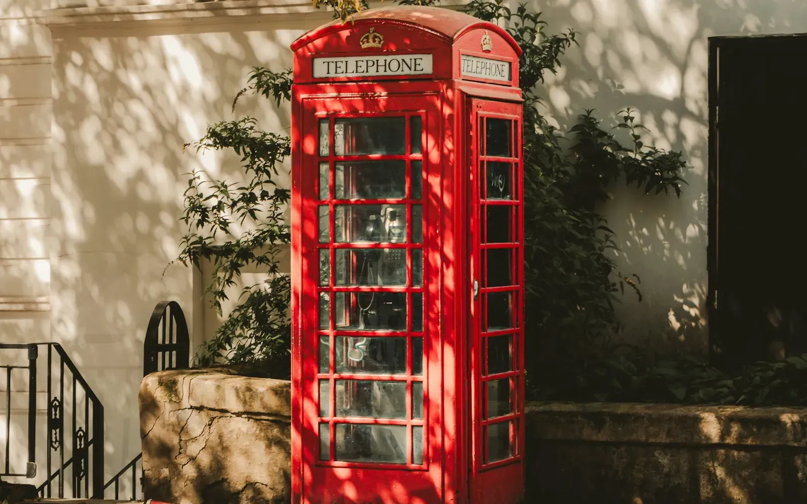 Rote britische Telefonzelle mit der Aufschrift Telephone vor einer sonnigen Hauswand mit Efeu